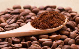 Coffee blend ground on spoon resting on pile of coffee beans